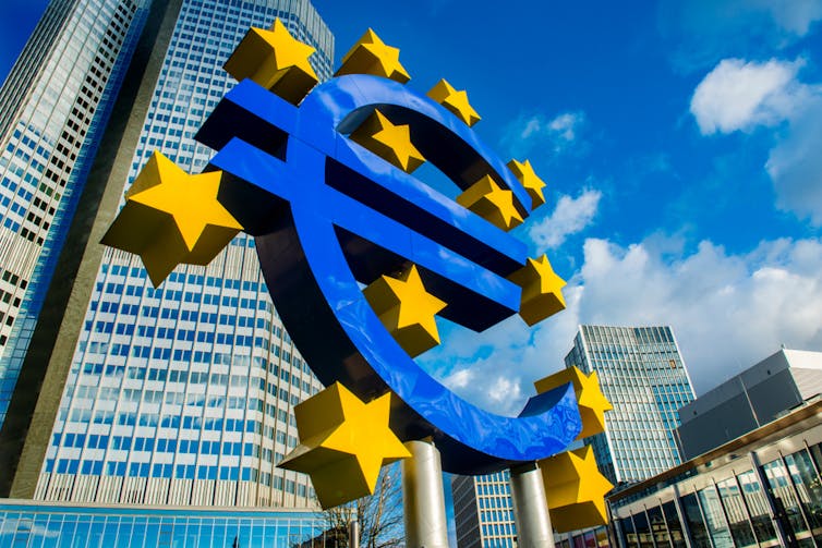 Großes blaues Euro-Schild vor dem Wolkenkratzer.
